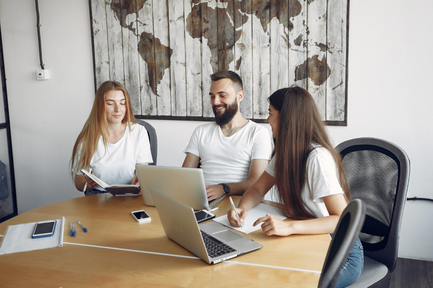 Trois personnes échangent autour d’une table avec leurs ordinateurs et carnets, dans une ambiance collaborative. Ce visuel illustre les formations professionnelles intra-entreprise proposées par Formasio, basées sur l’écoute, le partage et l’adaptation aux besoins des équipes.