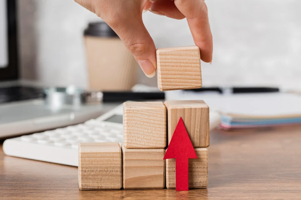 Main construisant une pyramide de blocs en bois avec flèche rouge ascendante, illustrant la formation professionnelle comme levier de croissance pour les entreprises.
