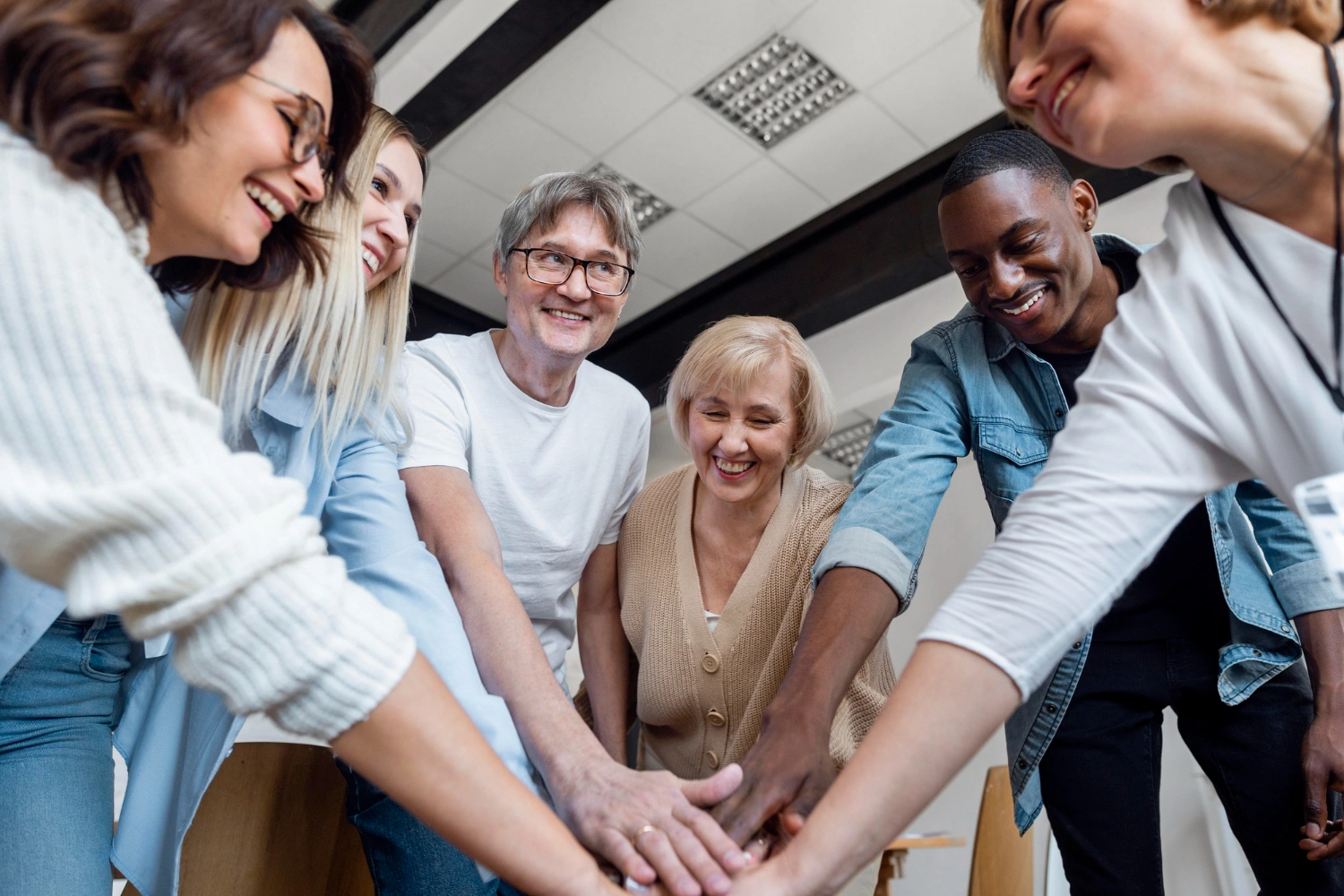 Groupe de personnes souriantes unissant leurs mains, illustrant la cohésion, la confiance et le développement personnel en milieu professionnel.