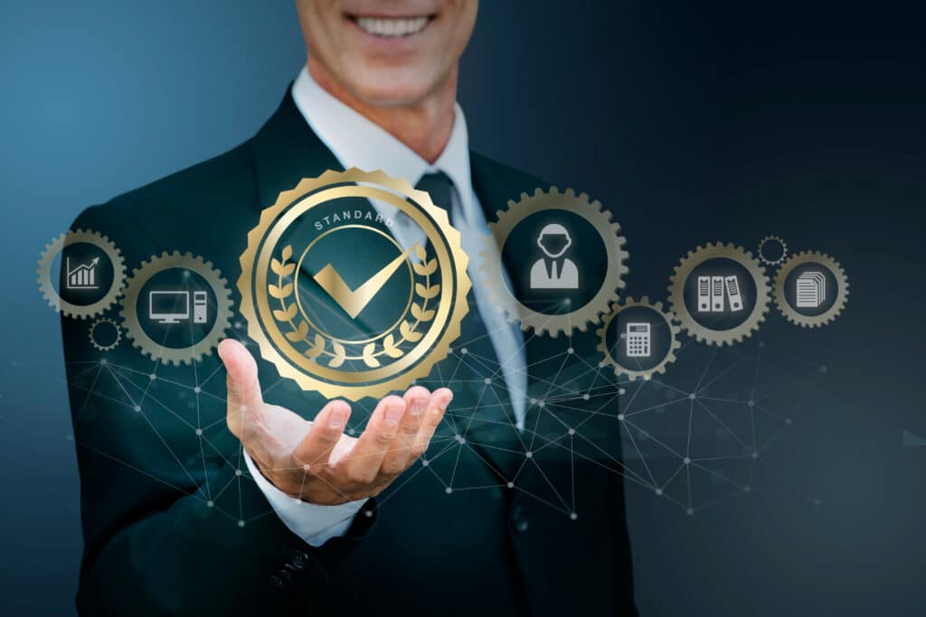 Homme d’affaires tenant une icône de certification qualité entourée de pictogrammes illustrant les processus, la conformité, la gestion documentaire et les standards professionnels.